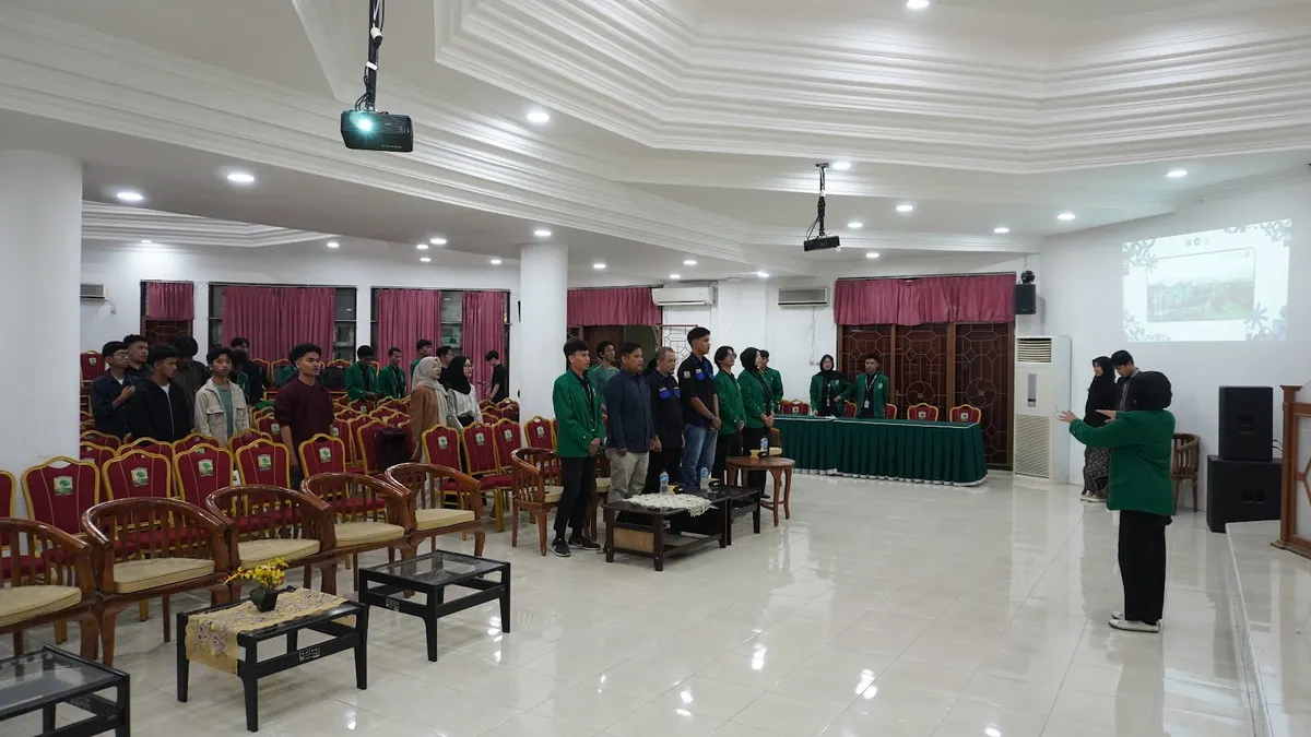 Pandangan luas ruang kegiatan dengan peserta, panggung, dan layar proyektor.