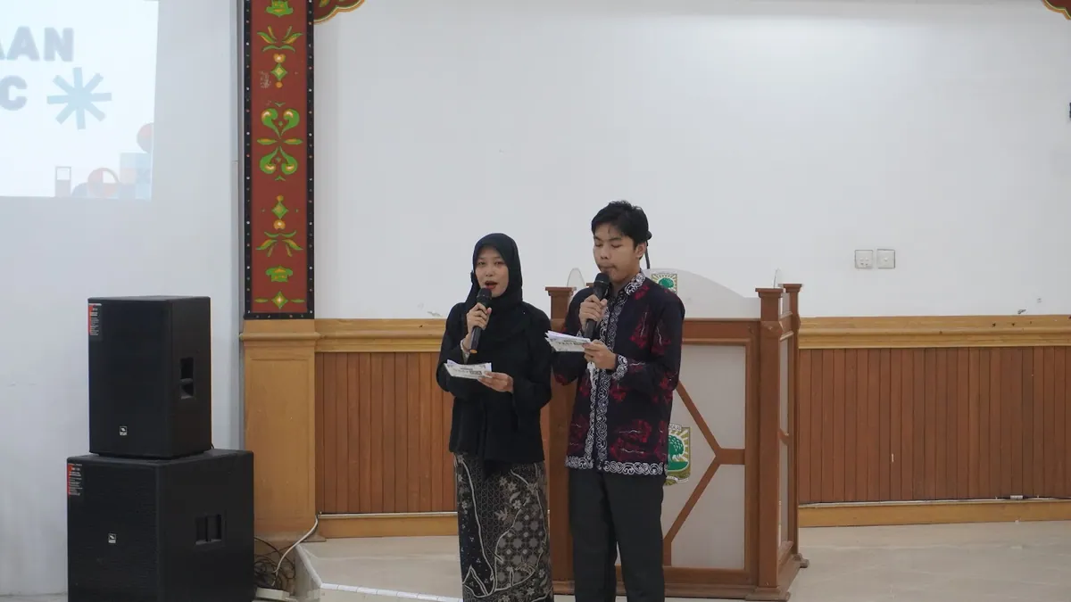 Dua pembawa acara menggunakan mikrofon di ruang seminar.
